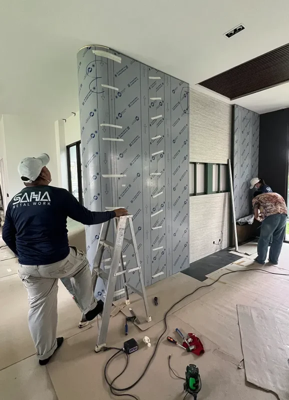 Expert contractor installing custom bronze satin stainless steel cladding on a massive bespoke TV cabinet during a Bangkok condo renovation.