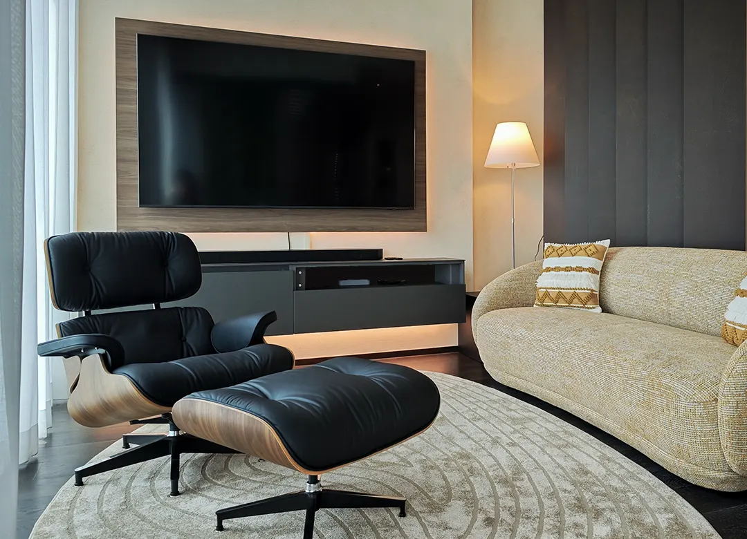 Luxury living room with curved sofa, Eames lounge chair, organic rug, and backlit TV feature wall at The Forestias Bang Na penthouse by Elementi Interiors