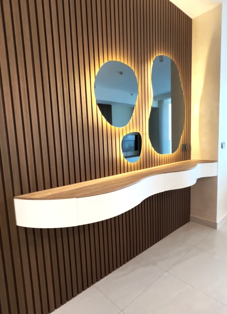 Custom floating curved entrance shelf with integrated drawer, slatted timber wall, and backlit organic mirrors at Tait Sathorn 12 by Elementi Interiors