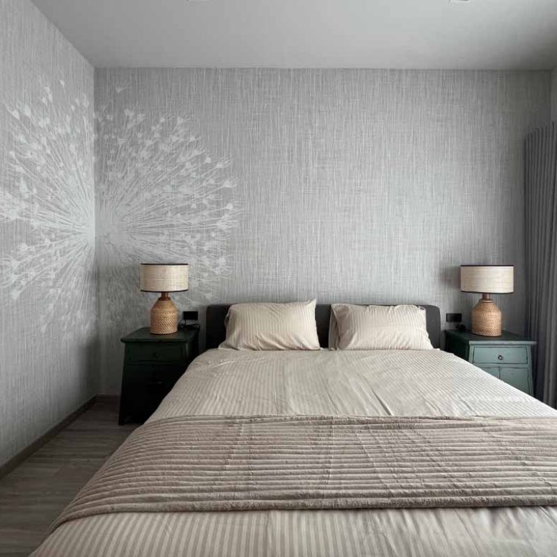 Soft neutral girl's bedroom at AIRI KM.5 by Elementi Interiors, featuring a bespoke Inkiostro Bianco textured wallpaper mural with a dandelion accent, neutral bed linens, vintage green nightstands, and woven table lamps.