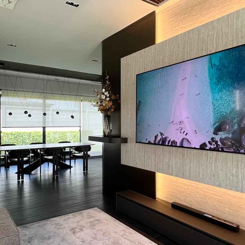 Modern open-plan living and dining room in the AIRI Km.5 project featuring a custom floating TV wall with ambient LED backlight, textured laminate travertine finish, and the Cattelan Italia Tyron Keramik dining table close to garden window.