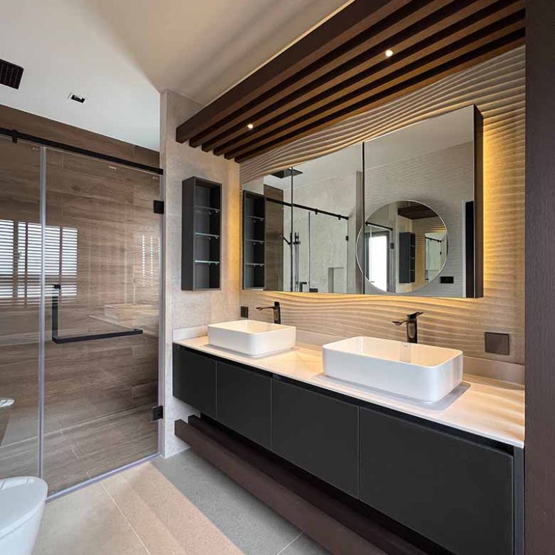 Angled view of a modern master bathroom vanity in the AIRI Km.5 project showcasing dark floating cabinets, white double vessel sinks, slatted timber canopy lighting, and a wave-textured Porcelanosa Samui 3D wave ceramic tile behind the mirror cabinet.