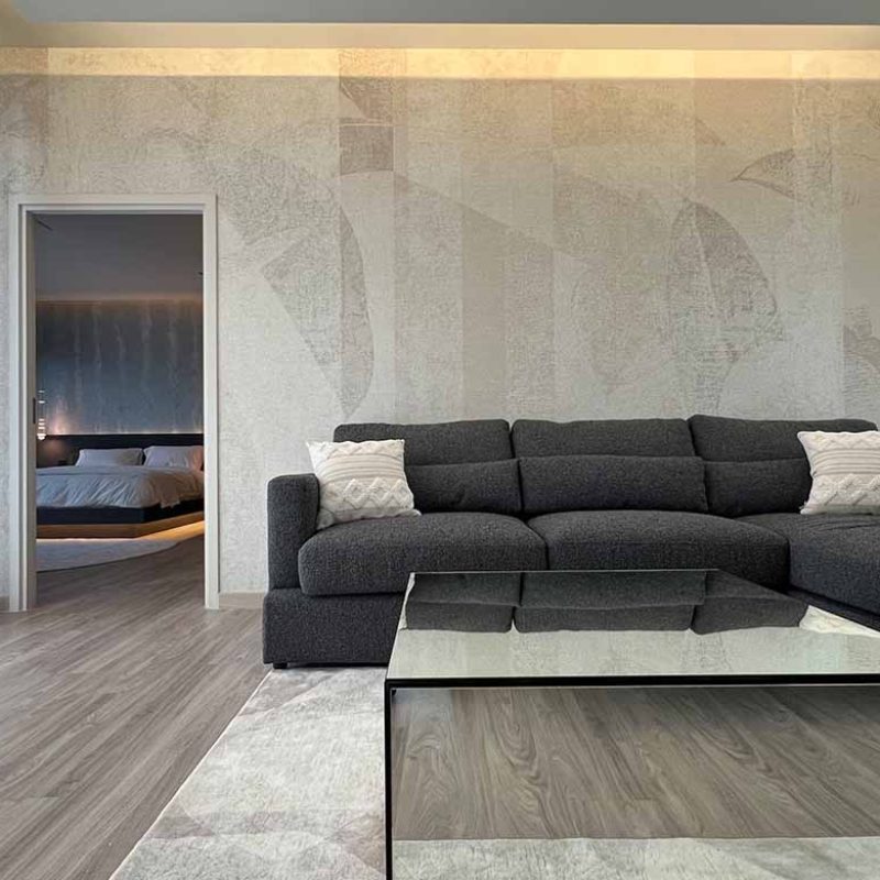 Modern playroom in the AIRI Km.5 project featuring an Inkiostro Bianco mural wallpaper feature wall, charcoal grey sectional sofa, mirrored coffee table, and an doorway view into the master bedroom.