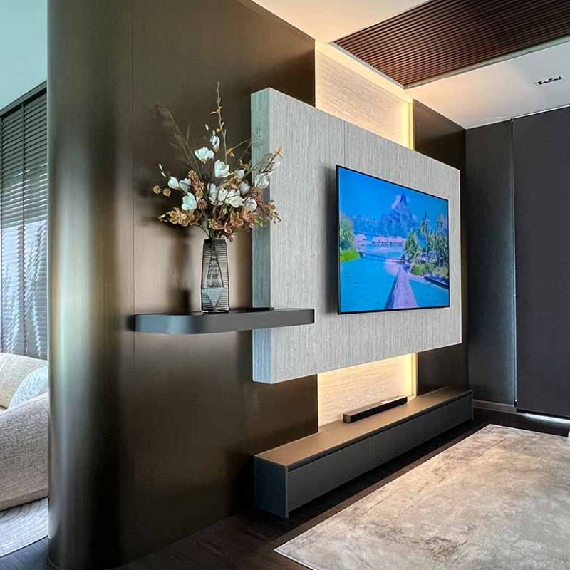 Bespoke TV wall feature in the AIRI Km.5 project by Elementi Interiors featuring curved bronze steel cladding, floating travertine laminate panel with indirect LED backlighting, and a dark low media console.