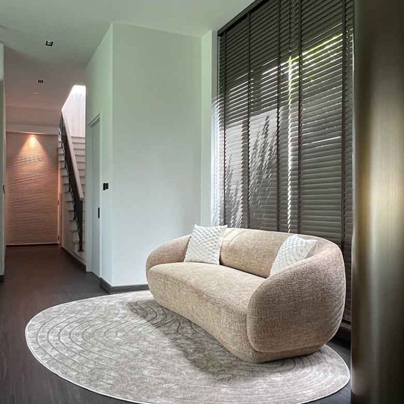 Modern living area featuring a beige curved boucle sofa on a pattern rug, dark wooden Venetian blinds, and a textured wave-patterned accent feature wall down the hallway.