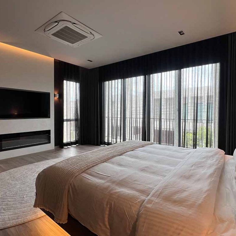 Master bedroom suite view at AIRI Km.5 by Elementi Interiors, featuring a white textured feature wall with a flush recessed TV and modern linear LED scenic fireplace, dark sheer drapery, and floating platform bed.